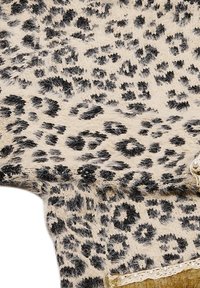 Leopardmönstrad tyg med en beige bas och svarta fläckar, med en texturerad, fluffig yta och spetsdekorationer längs kanten.