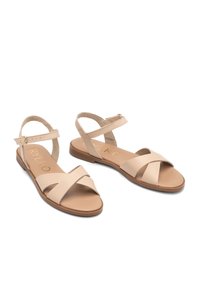 Beżowe płaskie sandały z krzyżującymi się paskami, tylnym paskiem na kostkę i wyściełaną wkładką. Wykonane z materiału syntetycznego o gładkiej fakturze.