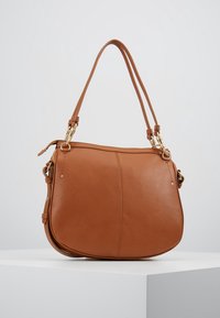 Brun læder skuldertaske med en buet form, dobbelte skulderstropper og hardware i gyldent tone. Glat tekstur uden synlige mønstre.