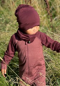 Maroon one-piece outfit with long sleeves and a high neckline, paired with a matching beanie. Soft, textured fabric, fitted design.