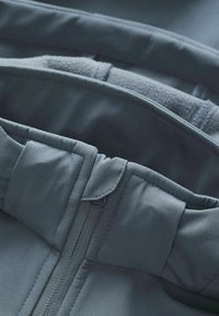 Giacca softshell leggera in blu scuro con fodera in pile, chiusura a zip e polsini elasticizzati. Tessuto liscio e resistente con texture sottile.