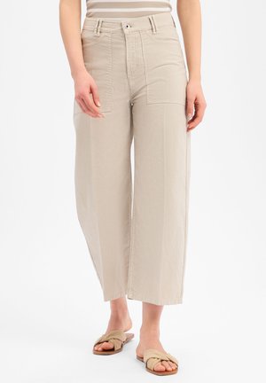 Beige weite, gekürzte Hosen mit aufgesetzten Fronttaschen, getragen mit beigen flachen Sandalen mit gedrehten Riemen und einem gestreiften Oberteil.