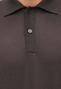 Polo grigia lavorata a maglia con texture a coste, dotata di colletto a risvolto e patta con due bottoni. I bottoni sono rotondi e di colore grigio scuro.