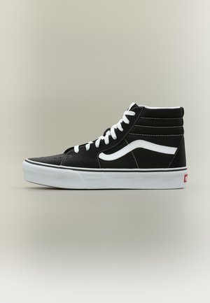 Baskets montantes noires avec lacets blancs, bande latérale blanche et semelle blanche sur un fond clair uni.