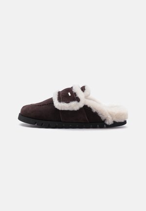Zapatilla de ante marrón oscuro con forro blanco y esponjoso y suela gruesa, con una correa ancha en la parte superior para un ajuste cómodo.
