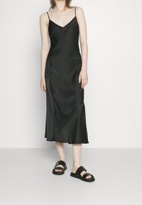 Svart satin slipklänning med tunna axelband, V-ringning och midilängd. Matchad med svarta sandaler som har ett guldaccent.