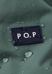 Vanddråber på grøn stof nær et mørkeblåt rektangel med hvide bogstaver "P.O.P" præget på det.