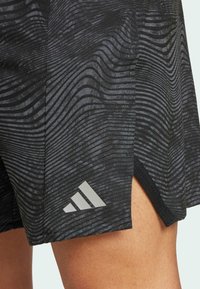 Crne sportske kratke hlače s reljefnim valovitom uzorkom, napravljene od prozračnog materijala. Uključuju sivi Adidas logo na donjoj strani.