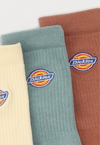 Τρία διπλωμένα ριγωτά καλτσάκια σε κρεμ, φιστικί και σκουριά χρώματα, το καθένα με στρογγυλό λογότυπο Dickies.