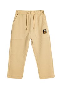 Pantalones de color beige con textura de waffle, con una cintura elástica y cordón, que cuentan con dos bolsillos laterales y un pequeño parche con el logo en el frente.