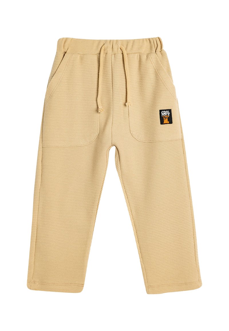 Pantalones de color beige con textura de waffle, con una cintura elástica y cordón, que cuentan con dos bolsillos laterales y un pequeño parche con el logo en el frente.