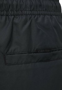 Pantaloni corti neri in tessuto leggero con cintura elastica. Presenta una tasca cucita e un piccolo etichetta del marchio Calvin Klein sul retro.