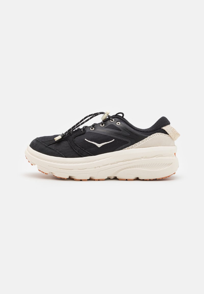 Sapatos atléticos pretos com um upper texturizado, atacadores elásticos e uma sola espessa de cor creme. Apresenta um logo discreto na lateral e detalhes no calcanhar.