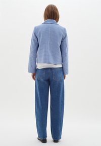 Chaqueta de cuadros vichy azul con un diseño cortado, combinada con unos jeans de denim azul de corte holgado, vista desde atrás. Cuello plano y herrajes simples.