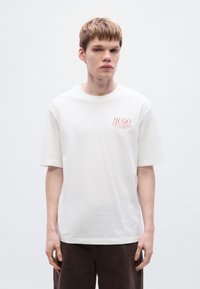 Λευκό βαμβακερό t-shirt με άνετη εφαρμογή. Διαθέτει κοντά μανίκια και κόκκινο λογότυπο τυπωμένο στο αριστερό στήθος. Λεπτή υφή.