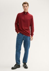 Roter Quarter-Zip-Pullover mit langen Ärmeln, kombiniert mit blauen Jeans und schwarzen Schnürschuhen. Glatte Textur, lässige Passform.