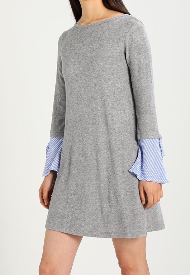 Grå stickad klänning med moderna, urtagna ärmar i blå och vita ränder. Rund halsringning och avslappnad passform som når till mitten av låret. Mjuk textur.