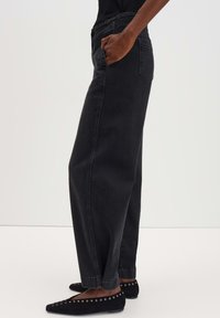 Schwarze Denim-Jeans mit einer lässigen Passform, mit geraden Beinen und Seitentaschen. Kombiniert mit schwarzen Ballerinas und einem schlichten Oberteil.