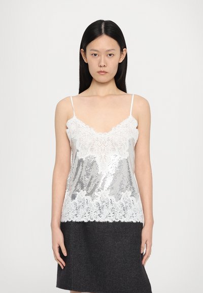 Lace-trimmet, sølvfarvet paillet camisole med tynde stropper; har en V-halsudskæring og en blondekant, båret over en mørk nederdel.
