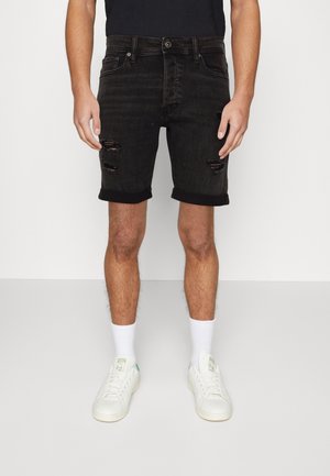 Schwarze Denim-Shorts mit ausgewaschenen Details und umgeschlagenen Säumen, kombiniert mit weißen Turnschuhen und Kniestrümpfen. Plattform und Design sind lässig.