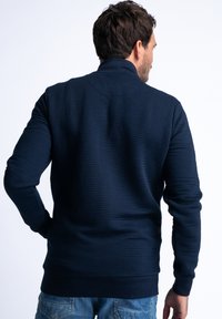 Navy sweatshirt with a textured ribbed pattern, high collar, and long sleeves. Features a fitted waistband and cuffs for a snug fit.