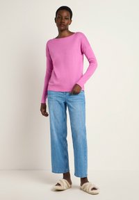Rosa Langarmpullover mit Bootsausschnitt, kombiniert mit hellblauen weiten Jeans und cremefarbenen, flauschigen Slidesandalen.