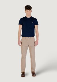 T-shirt attillato blu navy, chinos beige e scarpe da barca marroni. La T-shirt presenta un piccolo logo; i chinos hanno una chiusura con bottone e tasche.