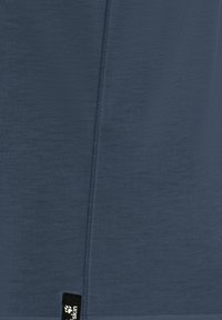 Κοντινό πλάνο σκούρου μπλε υφάσματος με κάθετη ραφή και μαύρη ετικέτα που φέρει λευκό αποτύπωμα πατούσας και μερικό κείμενο.