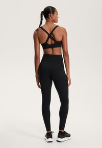 Črna športna nedrčka z križnimi naramnicami in zaponko. Črne legice z visokim pasom in gladko teksturo ter podrobnostmi šivov.