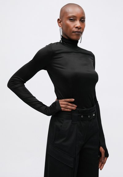 Pulover negru cu mânecă lungă și guler înalt, realizat dintr-un material neted și elastic, asociat cu pantaloni negri cu talie înaltă, având o buză mare.