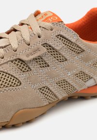 Beige sko med mesh- og semsket lædermaterialer, med orange detaljer, teksturert gummi såle og snøring. Diskret logo detalj på siden.