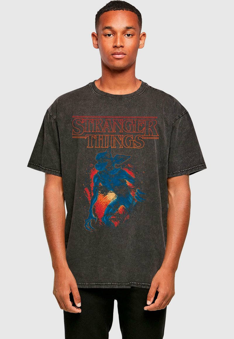 T-shirt oversize noir avec un imprimé graphique coloré de créature issu de "Stranger Things", col rond et manches courtes.