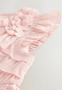 Heleroosa kleit, millel on kihilised volangid, südamekujulised aplikatsioonid ja pehme tekstuur. Sisaldab õrna serva ja volangidega detaile.