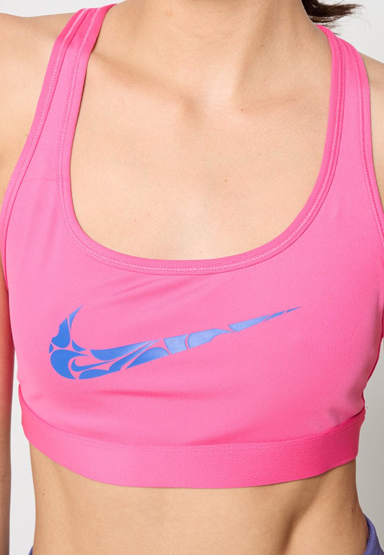 Mujer vestida con un sujetador deportivo de color rosa brillante con un logotipo de Nike azul con patrón en la parte frontal, cortado para mostrar el torso y el escote.