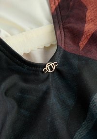 Tissu noir à motifs colorés avec une texture lisse. Comprend un détail en métal doré décoratif près de l'encolure.