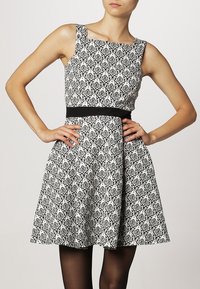 Abito a fantasia in bianco e nero con scollatura quadrata, corpino aderente e gonna a ruota. Presenta una cintura nera a contrasto in vita.