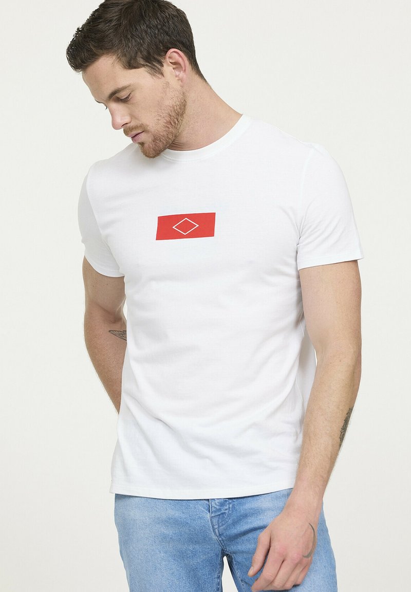 T-shirt en coton blanc avec un graphisme rectangulaire rouge au centre en forme de diamant. Manches courtes et encolure ras du cou.