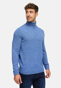 Hellblauer Rollkragenpullover aus Strickstoff, mit langen Ärmeln und gerippten Bündchen und Saum. Kombiniert mit dunklen Jeans.