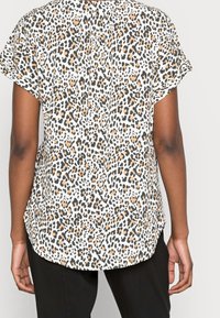 Blusa a maniche corte in tessuto leggero, con stampa leopardata in nero, arancione e bianco, dotata di orlo curvo e dettaglio con piega sul retro.
