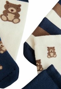 Calze con una base color crema e strisce blu navy, decorate con motivi di orso bruno sulle sezioni crema e con punte blu navy solide.