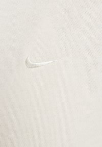 Maglietta Nike grigio chiaro con tessuto testurizzato. Include un piccolo logo ricamato tono su tono sul petto. Design semplice e minimalista.