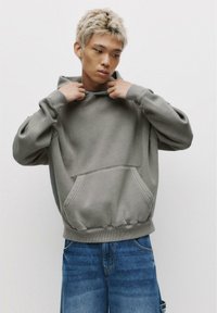 Gray hoodie made from soft fabric, featuring a front pocket, ribbed cuffs, and a drawstring at the hood. Worn with loose-fitting blue jeans.