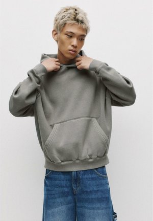 Gray hoodie made from soft fabric, featuring a front pocket, ribbed cuffs, and a drawstring at the hood. Worn with loose-fitting blue jeans.
