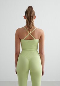 Limegrønn yogakolleksjon har en ribbet tekstur, en tettsittende crop top med kryssede stropper, og høytlivet leggings med en glatt overflate.