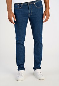 Dżinsy w ciemnoniebieskim kolorze o dopasowanym kroju, z prostymi nogawkami, subtelnym efektem przecierania oraz mosiężnymi dodatkami. W zestawie z białymi trampkami.