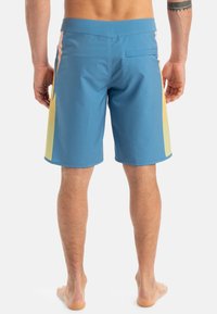 Pánske plavky modrej farby s žltými a ružovými bočnými pruhmi, elastickým pásom, zadným vreckom a hladkým, ľahkým materiálom.