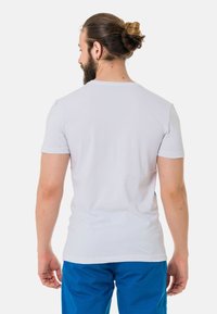 Weißes T-Shirt mit kurzen Ärmeln und geripptem Rundhalsausschnitt, aus weichem Baumwollmaterial, von hinten gesehen, kombiniert mit blauen Shorts.