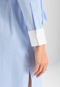 Baumwollhemd mit hellblauen und weißen vertikalen Streifen. Weiße Manschetten mit Knopfdetails, seitlicher Schlitz im Saum für mehr Bewegungsfreiheit.