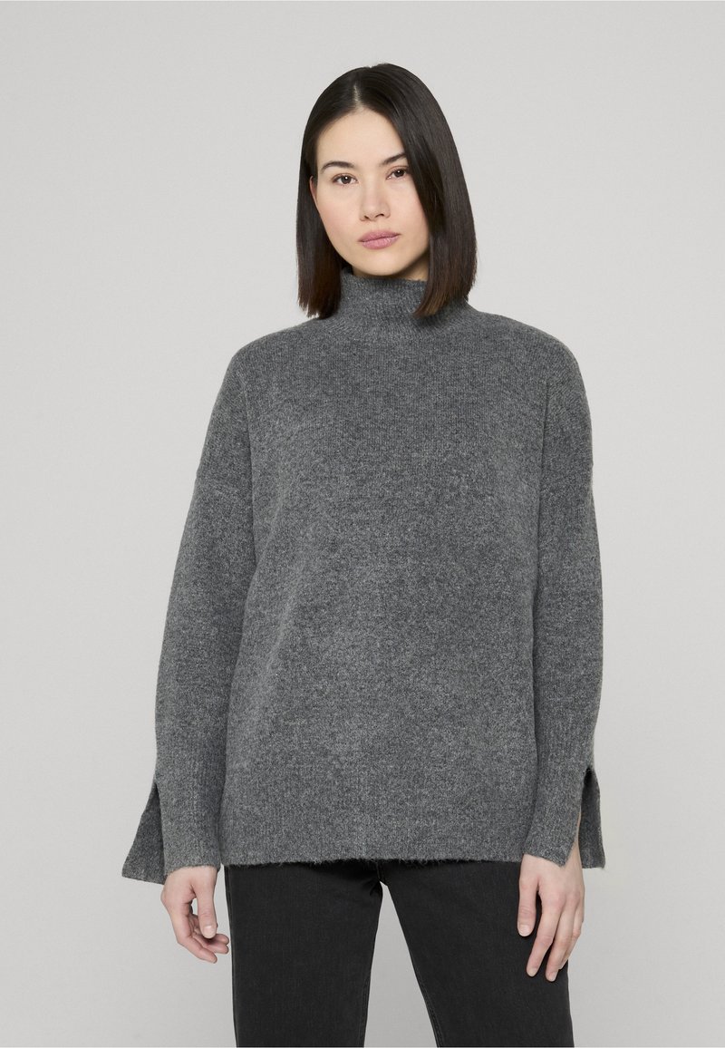 Pull gris en maille avec un col roulé haut, une coupe ample, des fentes latérales à l'ourlet, et une texture douce. Assorti à un pantalon noir.