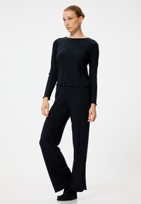 Zwart geribbeld loungewear set bestaande uit een top met lange mouwen en een wijde broek met een relaxte pasvorm en subtiele textuur.